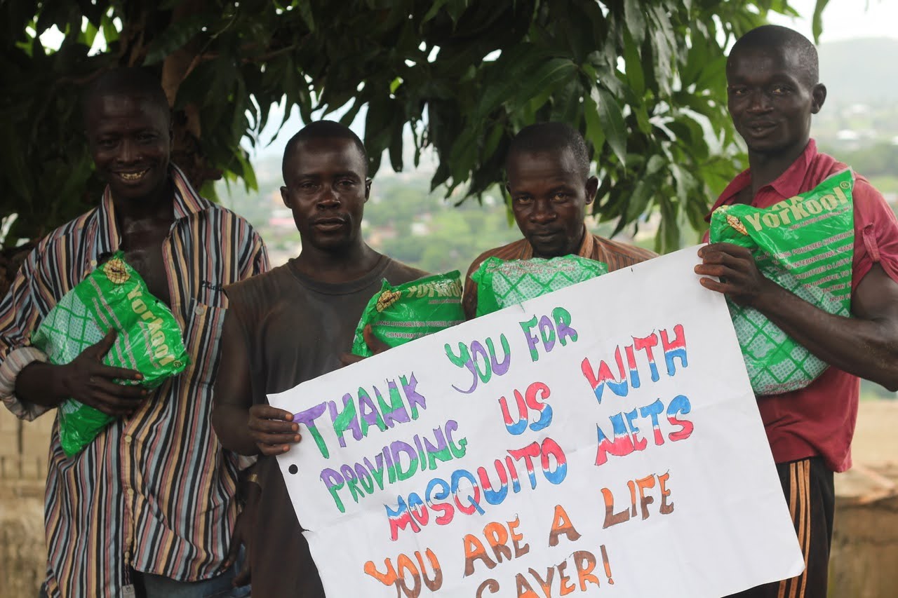 (c) Develop Africa. Four adults with a card thanking Develop Africa for saving their lives by providing mosquito net for them.