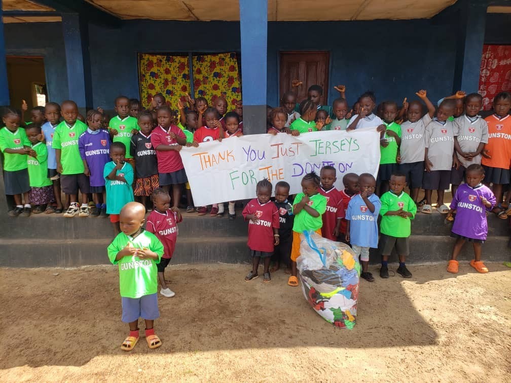 Kids in Kamawornie with jersey and banner thanking Develop Africa for the jersey.