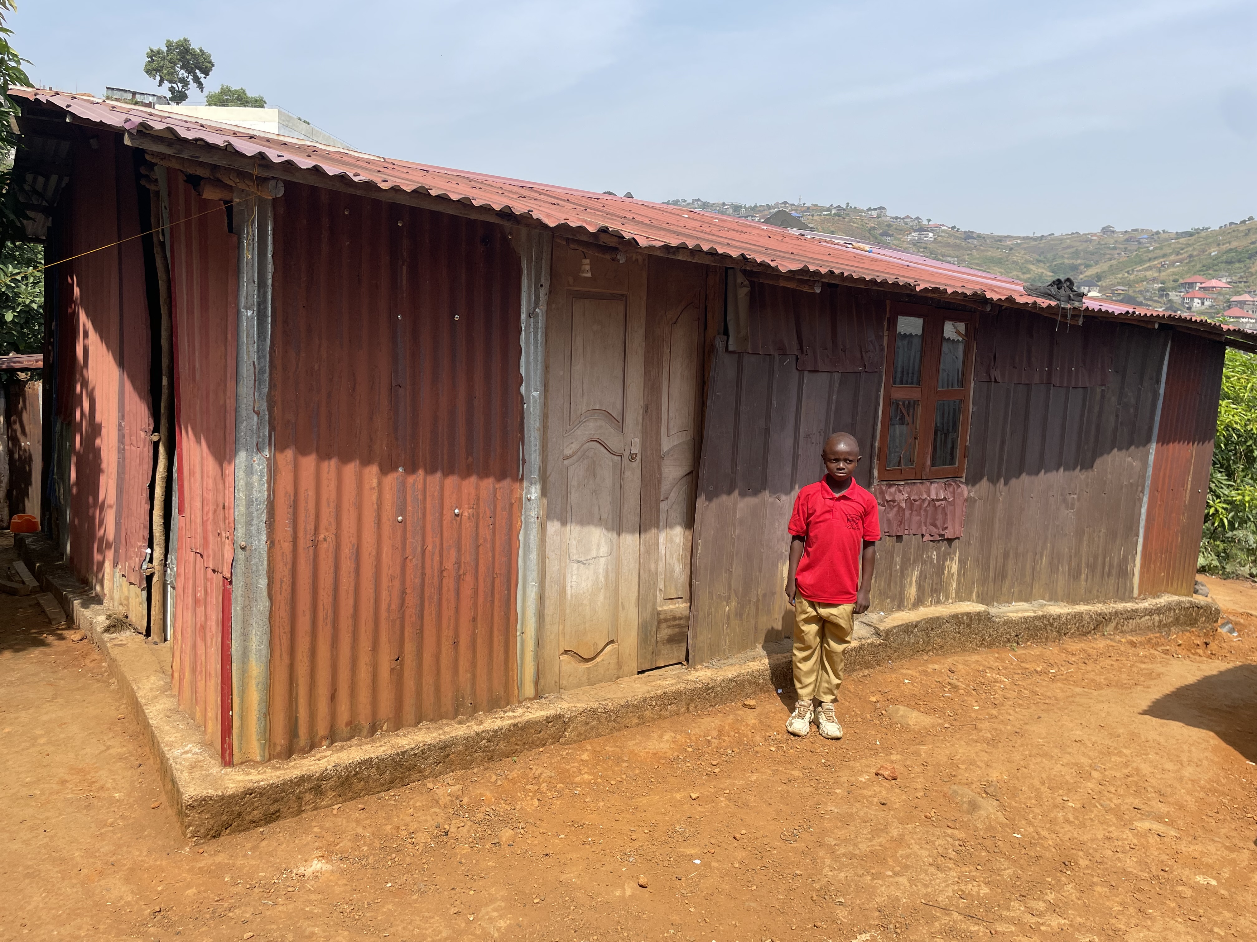 isaiah Koroma a beneficiary of develop africa standing outside his parents' home