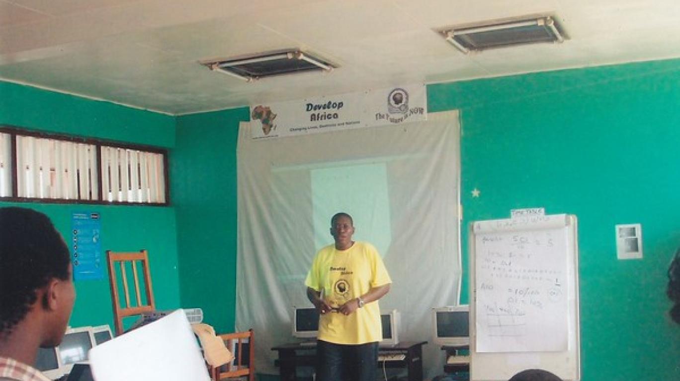 Sylvester - President & Founder of Develop Africa in a yellow T-Shirt in front of a training room in the early days of Develop Africa 