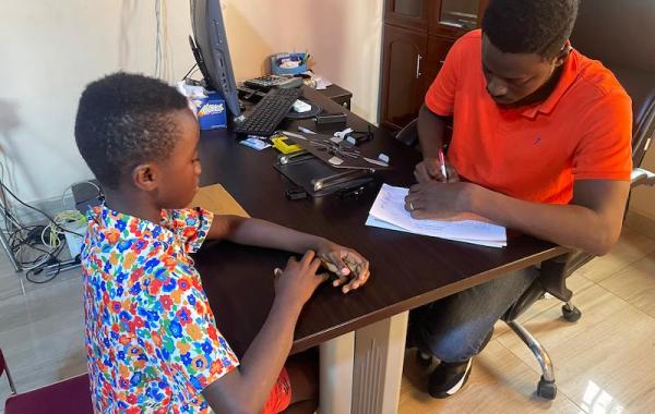 Joseph reviewing a beneficiary's report sheet, Sierra Leone, 2026