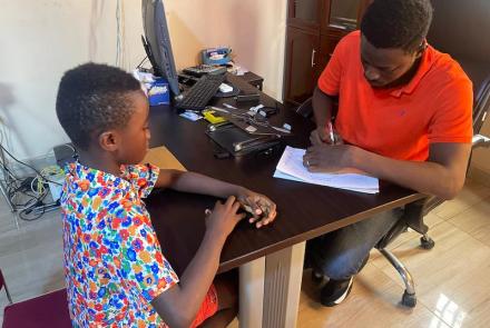 Joseph reviewing a beneficiary's report sheet, Sierra Leone, 2026